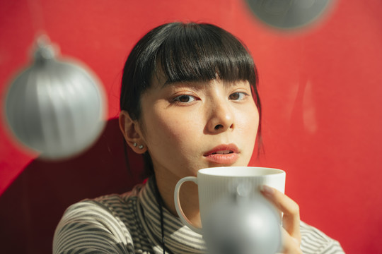 特写肖像-美丽的亚泰黑色长发女子拿着咖啡杯在红色背景。