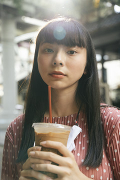美丽的亚泰长黑发女子在街上喝着冰凉的咖啡杯。