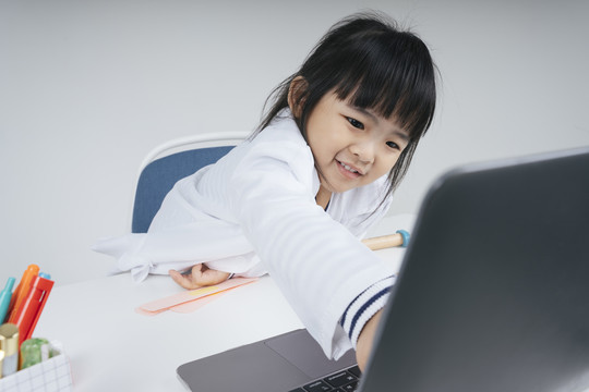 漂亮的泰国亚裔小孩扮演一个医生在笔记本电脑显示器屏幕上指出的角色。
