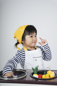 漂亮的泰国亚裔小孩扮演厨师的角色，戴着黄色绷带，在厨房里用炉子做饭。
