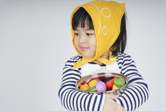 漂亮的泰国亚裔小孩扮演一个女招待，戴着黄色绷带，抱着白色背景的烹饪锅。
