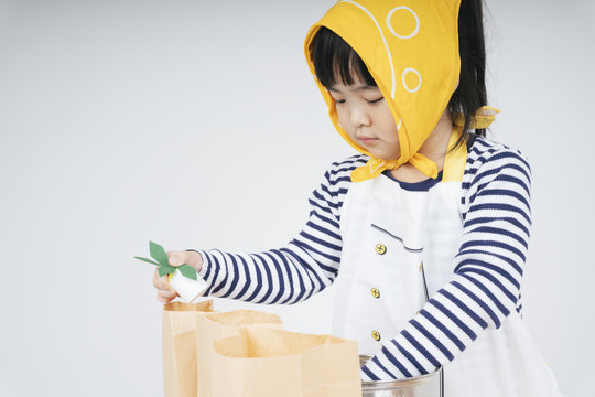 漂亮的泰国亚裔小孩扮演一个穿着黄色绷带的服务员，用纸袋包装食物。