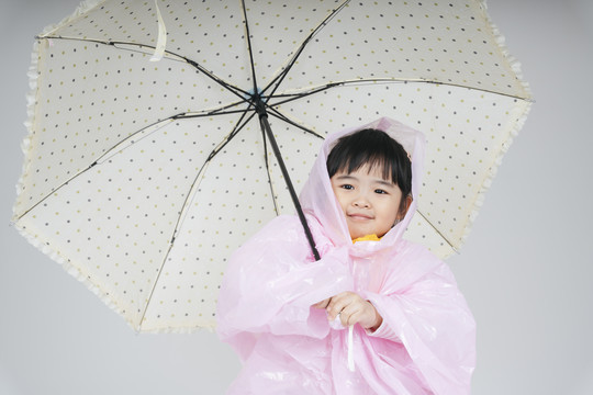 漂亮的泰国亚裔小孩，穿着粉色雨衣，撑着伞。