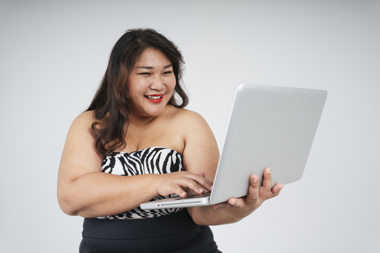 快乐的亚洲胖乎乎的女商人在白色背景下使用笔记本电脑的肖像。
