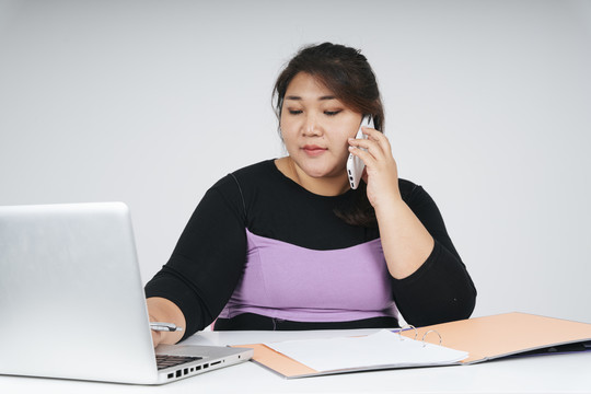 亚洲胖乎乎的女商人在笔记本电脑上工作，和顾客打电话