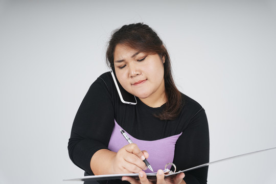 忙碌的亚洲胖乎乎的女商人在打电话和写文件。
