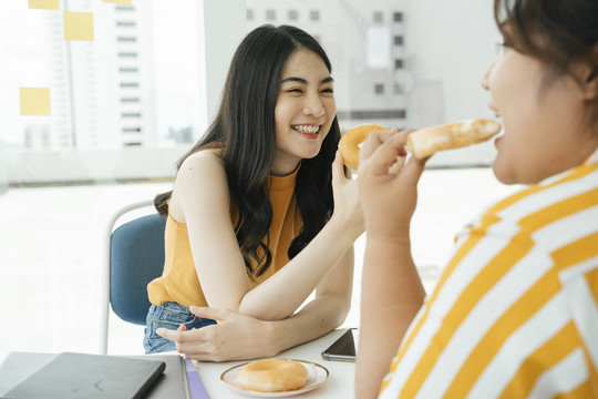 美丽的亚洲女人和朋友一起吃甜甜圈当午餐。
