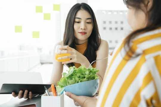 美丽的亚洲女人和朋友吃健康的食物，橙汁和沙拉。