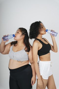 亚洲胖乎乎的非洲妇女穿着运动胸罩从白色背景的瓶子里喝水。