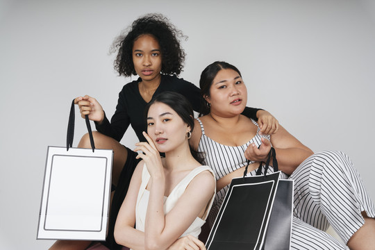 三位不同女性的集体肖像，亚裔和非洲人拿着购物袋做模型。