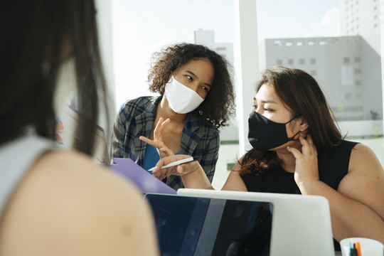三位不同的亚非商界女性戴着面具一起在办公室工作。