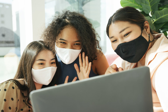 一群不同的女人戴着面具在家里用笔记本电脑做流媒体。