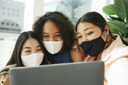 一群不同的女人戴着面具在家里用笔记本电脑做流媒体。