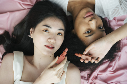 非洲和泰国妇女在粉色背景下拿着化妆品口红。