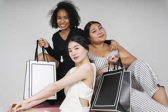 三位不同女性的集体肖像，亚裔和非洲人拿着购物袋在白色背景上做模型。