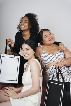 三位不同女性的集体肖像，亚裔和非洲人拿着购物袋在白色背景上做模型。