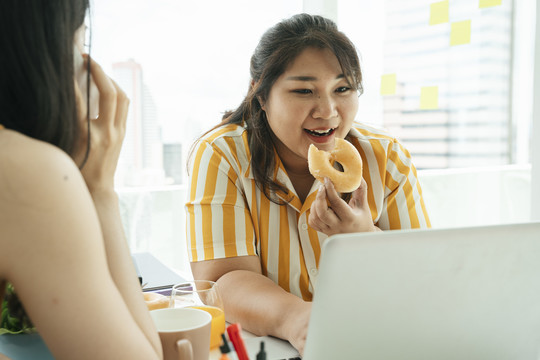 肥胖的商业女性午餐吃不健康的甜甜圈。