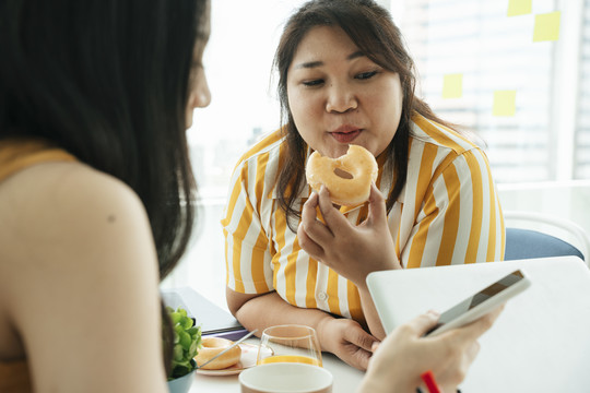 肥胖的商业女性午餐吃不健康的甜甜圈。