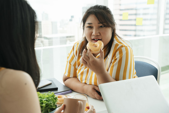 肥胖的商业女性午餐吃不健康的甜甜圈。