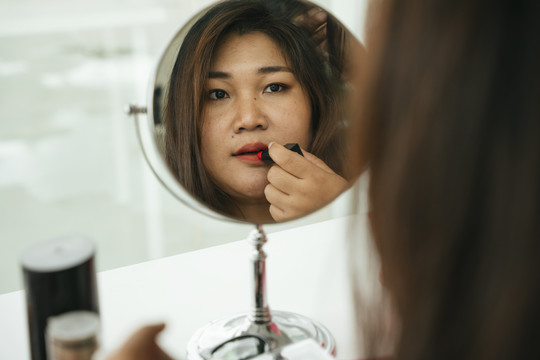 亚洲商人在化妆台前对着镜子涂口红。