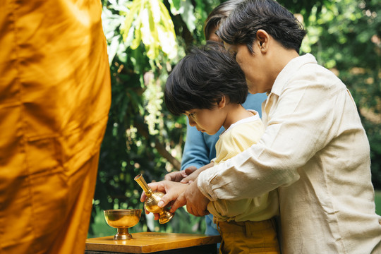 一个亚裔家庭在向僧侣施舍后从金杯里倒水。