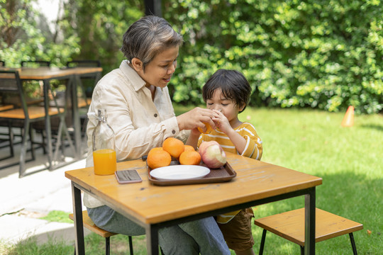 祖母和孙子喜欢在户外的公园里喝健康的有机橙汁。