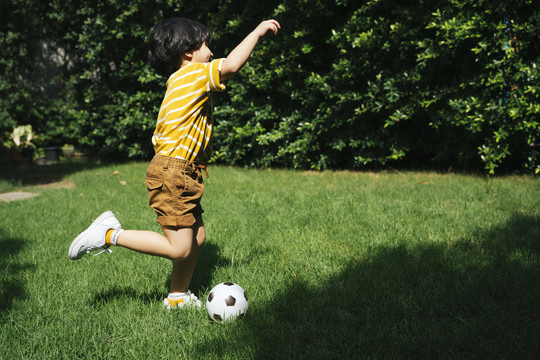 亚洲男孩的腿在公园的绿地上用足球奔跑和射击。