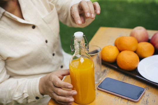 老妇人拿着橙汁瓶在公园户外野餐。