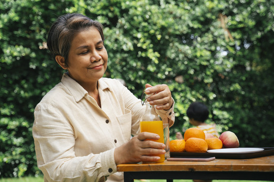老妇人在公园户外打开橙汁玻璃瓶。