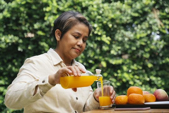 在公园里，一位年长的老妇人正在从户外的玻璃瓶里倒橙汁。