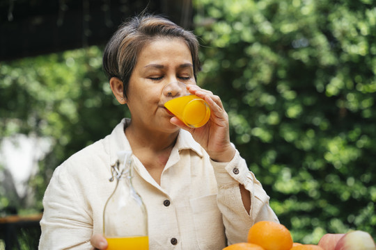 在公园户外喝玻璃杯橙汁的老年妇女。
