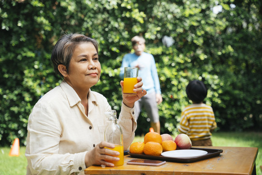 老年妇女喜欢在公园户外用玻璃杯喝橙汁。