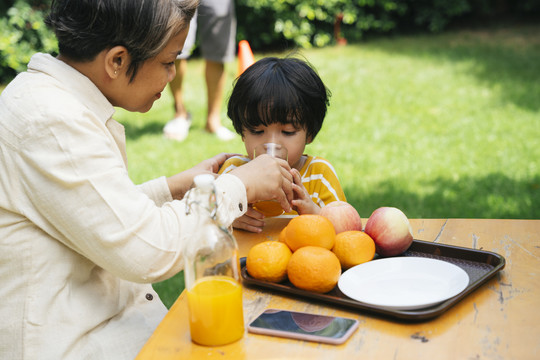 亚裔祖母和孙子一起在公园喝橙汁。