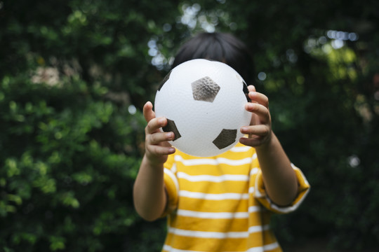 穿着黄衬衫的亚洲男孩在公园里踢足球的肖像。