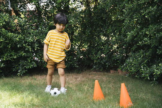 亚洲男孩在草地上用圆锥体练习运球。