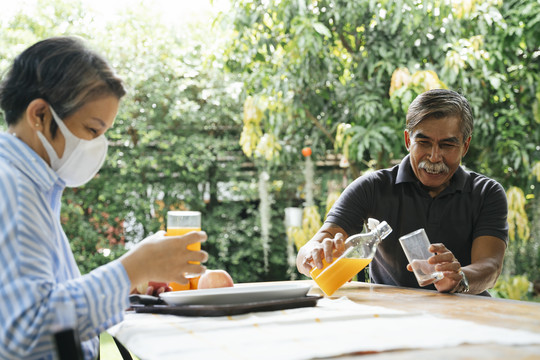 亚洲老人在院子里一起喝橙汁。