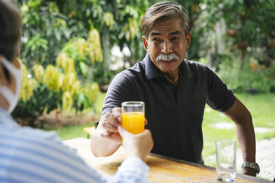 在户外院子里，一位年长的老人给妻子一杯橙汁。