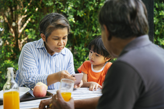祖父母和孙子在院子里学习如何在户外使用智能手机。