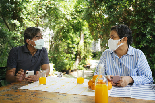 祖父母戴着面具在院子里野餐，桌上放着橙汁。