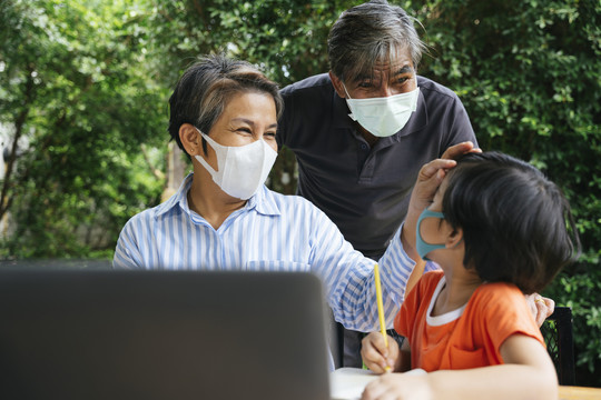 快乐的亚洲外孙父母和外孙戴着口罩一起在院子里做户外活动。