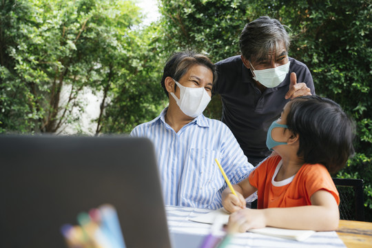 快乐的亚洲外孙父母和外孙戴着口罩一起在院子里做户外活动。