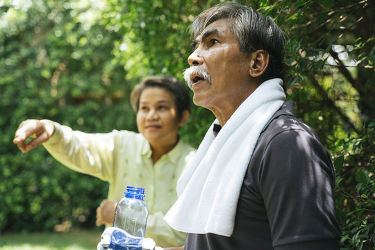亚洲老年夫妇一起在公园锻炼。老妇人指着什么东西。