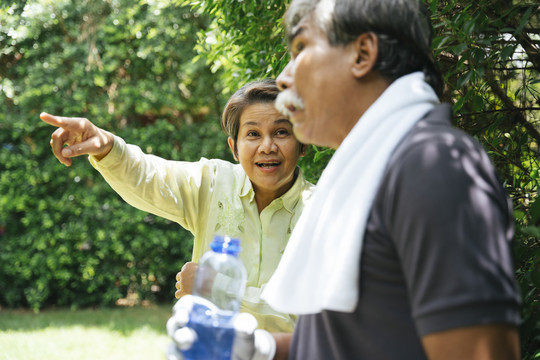 亚洲老年夫妇一起在公园锻炼。老妇人指着什么东西。
