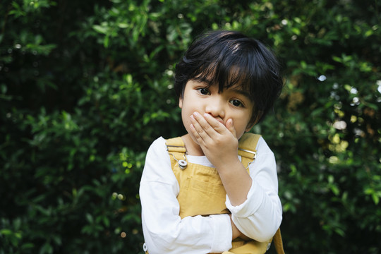 亚洲黑发小孩在院子里用手捂住嘴。