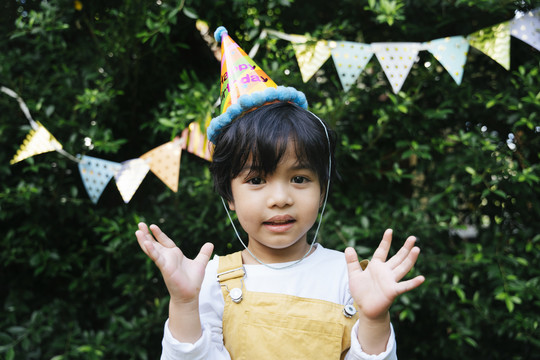 快乐的亚洲黑发孩子的画像戴派对帽在院子里庆祝生日。