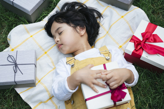俯视图-亚洲黑发儿童与生日礼物盒睡在草地上。