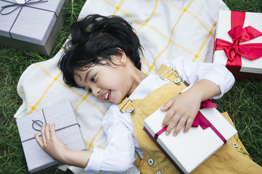 俯视图-亚洲黑发小孩躺在草地上，手里拿着生日礼物盒。