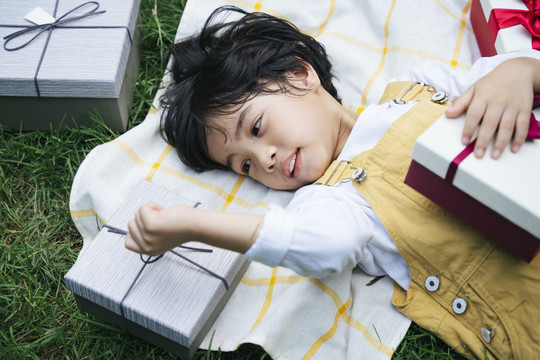 俯视图-亚洲黑发小孩躺在草地上，手里拿着生日礼物盒。