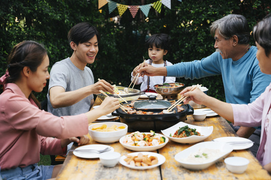 快乐的亚洲家庭喜欢在院子里一起吃泰国烧烤和当地食物。