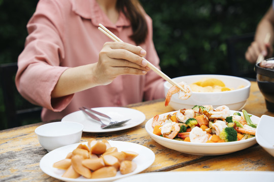 女人用筷子吃炒菜和香肠。